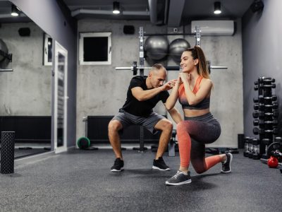 The concept of sports personal training. A fit man and a slender woman do sports exercises together. The lady stepped forward with her foot as the coach corrected her body position